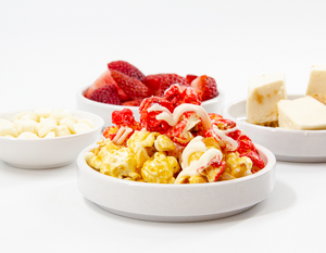 Mushroom Popcorn Kernels in candy Strawberry Cheesecake flavor drizzled in White Chocolate. Fresh Strawberries, Sweet, Creamy Cheesecake with graham cracker crust and white chocolate morsels surround popcorn.