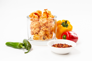 Hot & Spicy Gourmet Popcorn displayed with fresh jalapenos, spicy red pepper seasoning and bright red and yellow peppers.